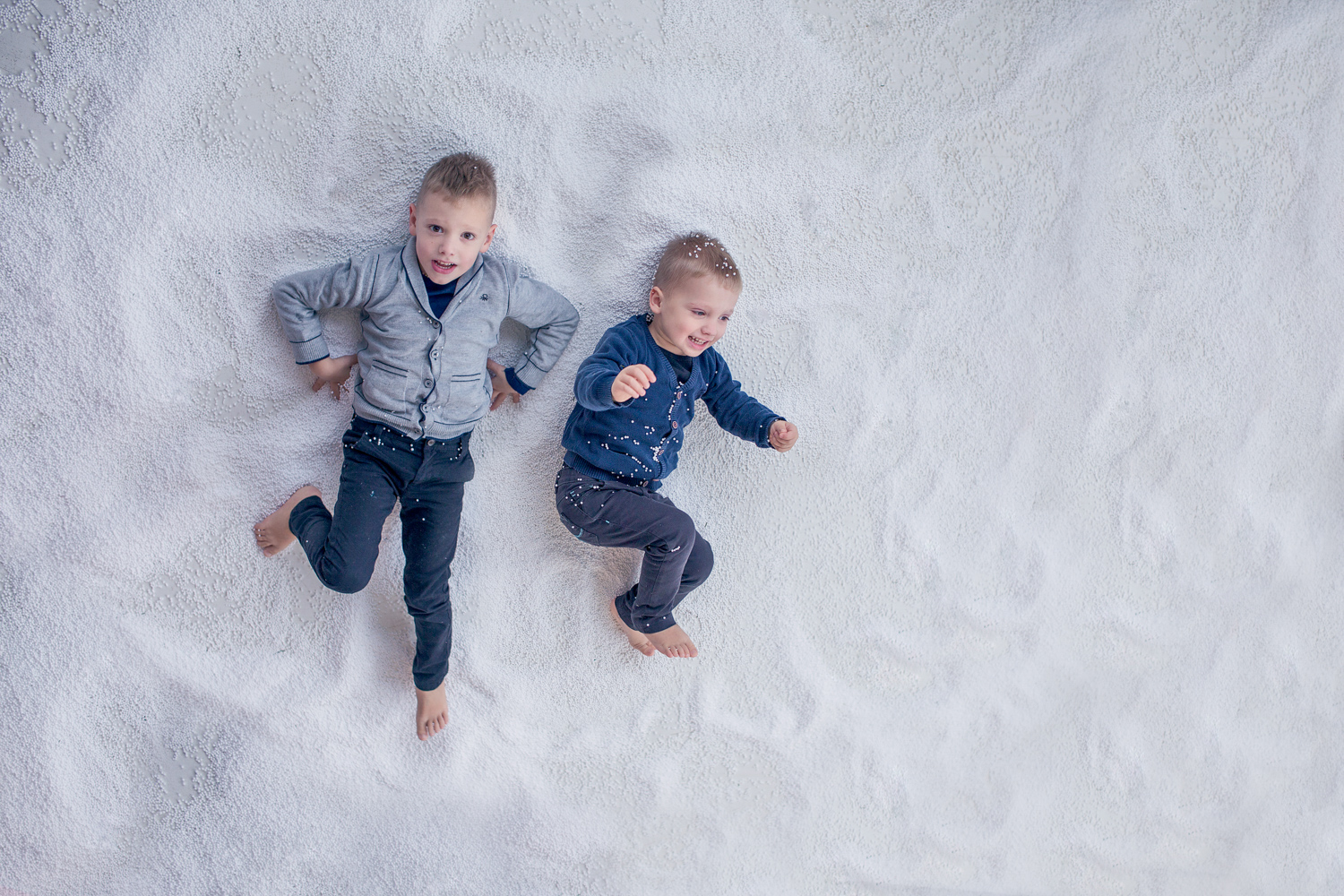 vaikai guli ant balto dirbtinio sniego Kalėdinėje fotosesijoje