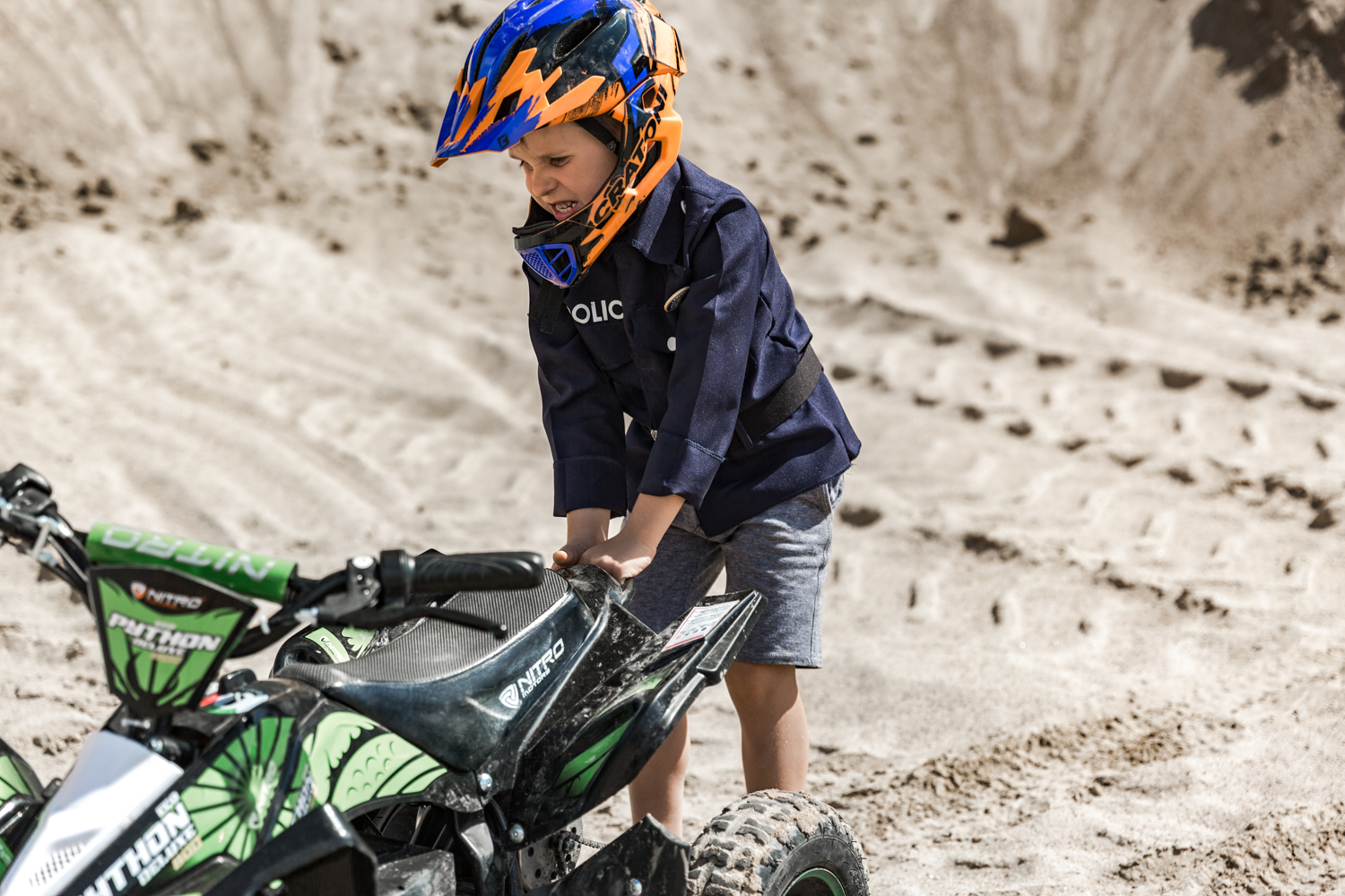 Berniukas su vaikiška policininko apranga traukia žalią keturratį