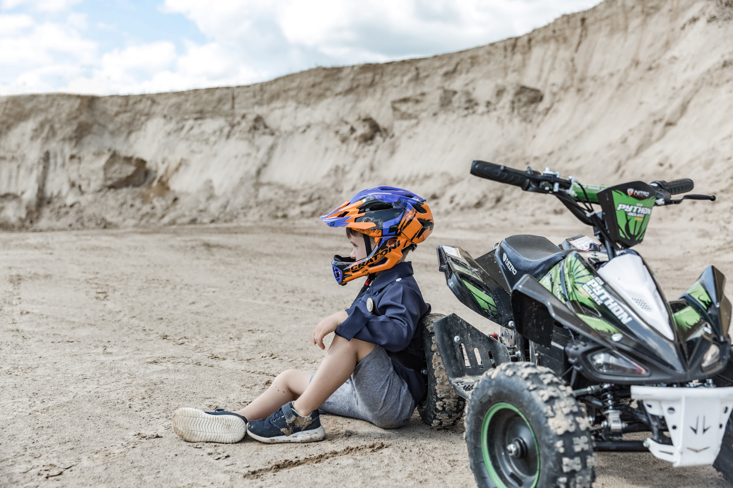 Vaikas sėdi prie keturračio smėlio karjere