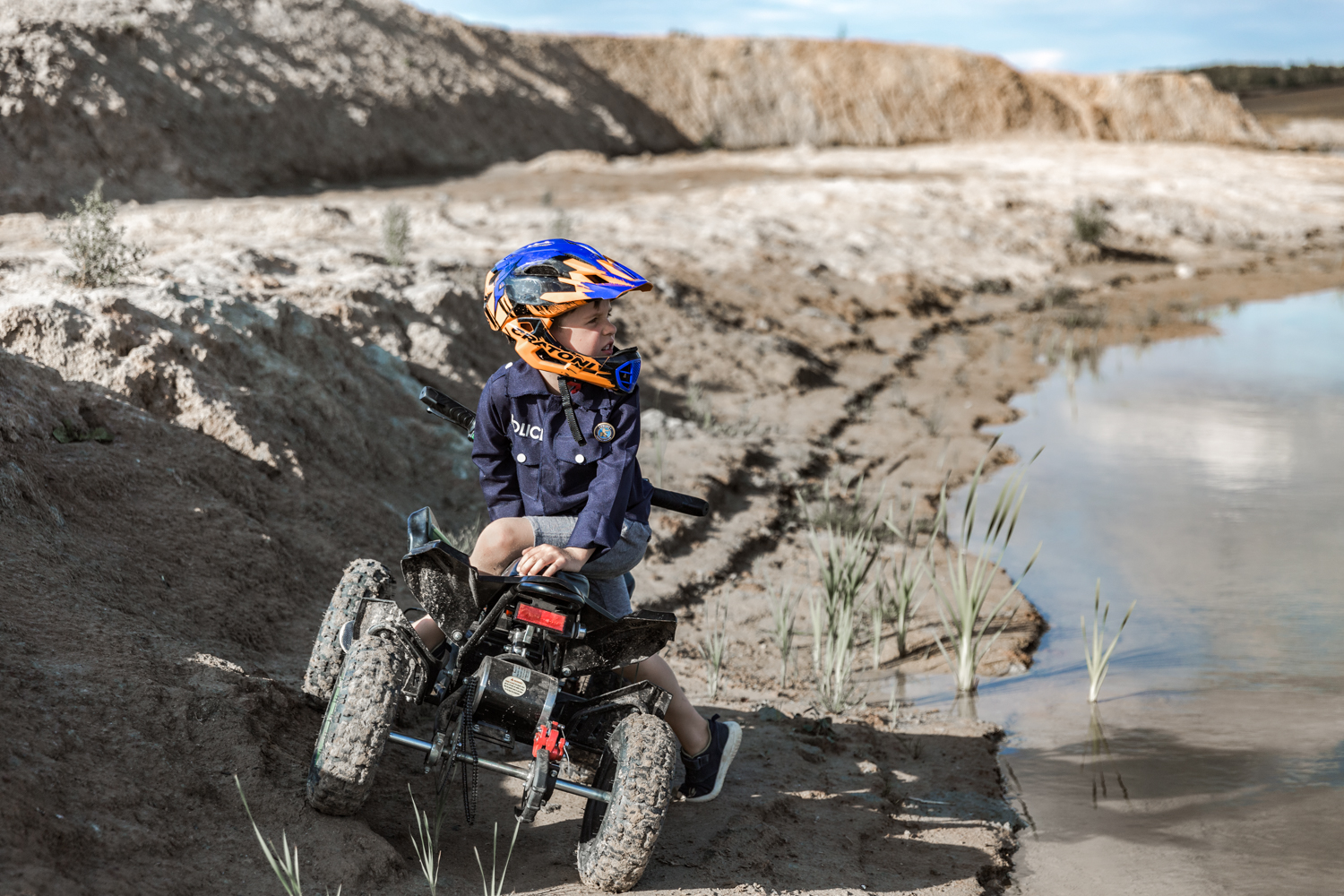 Berniukas su šalmu ant keturračio važiuoja per purvą šalia ežero