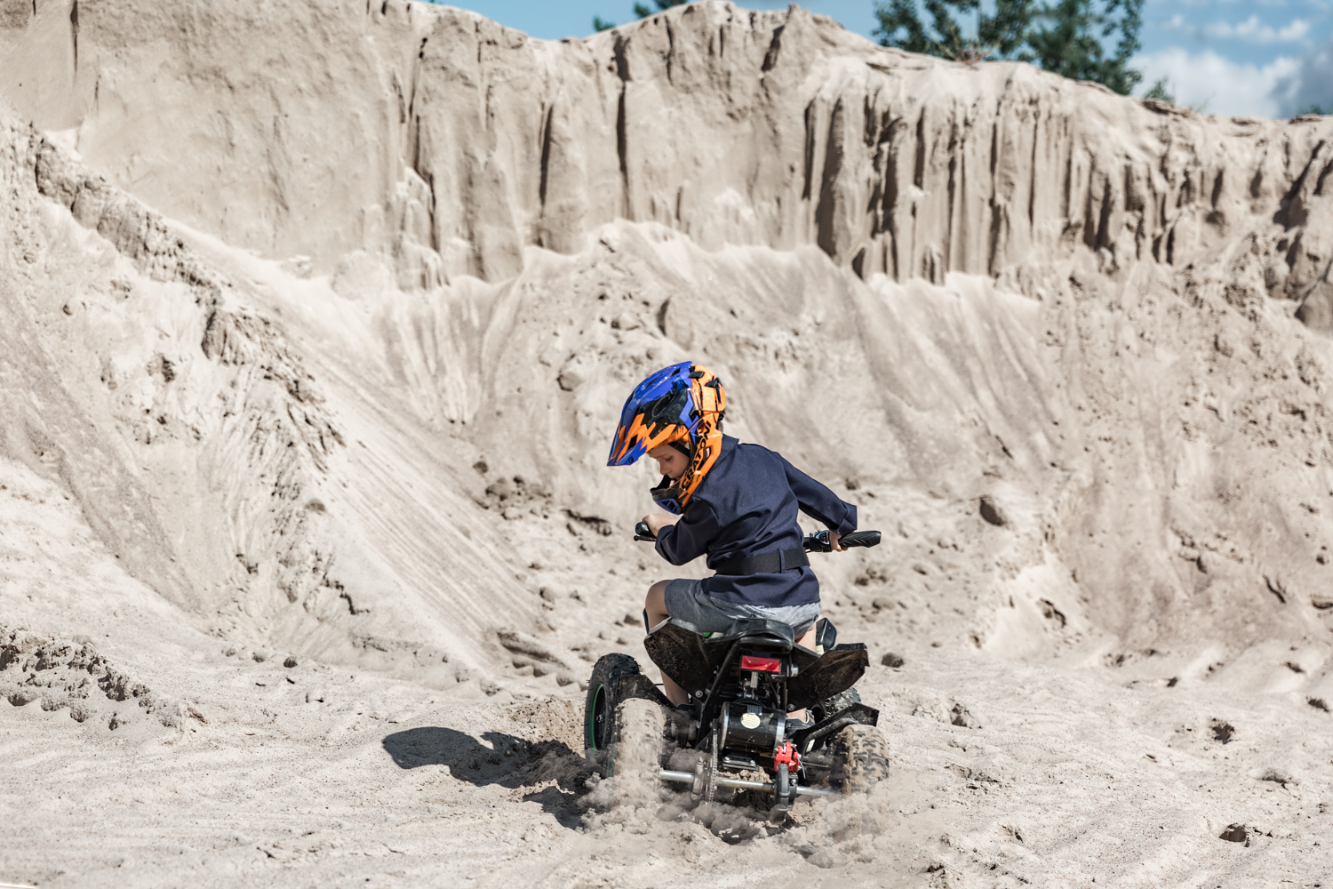 Vaikas su keturračiu važiuoja smėlio karjere per gimtadienio fotosesiją