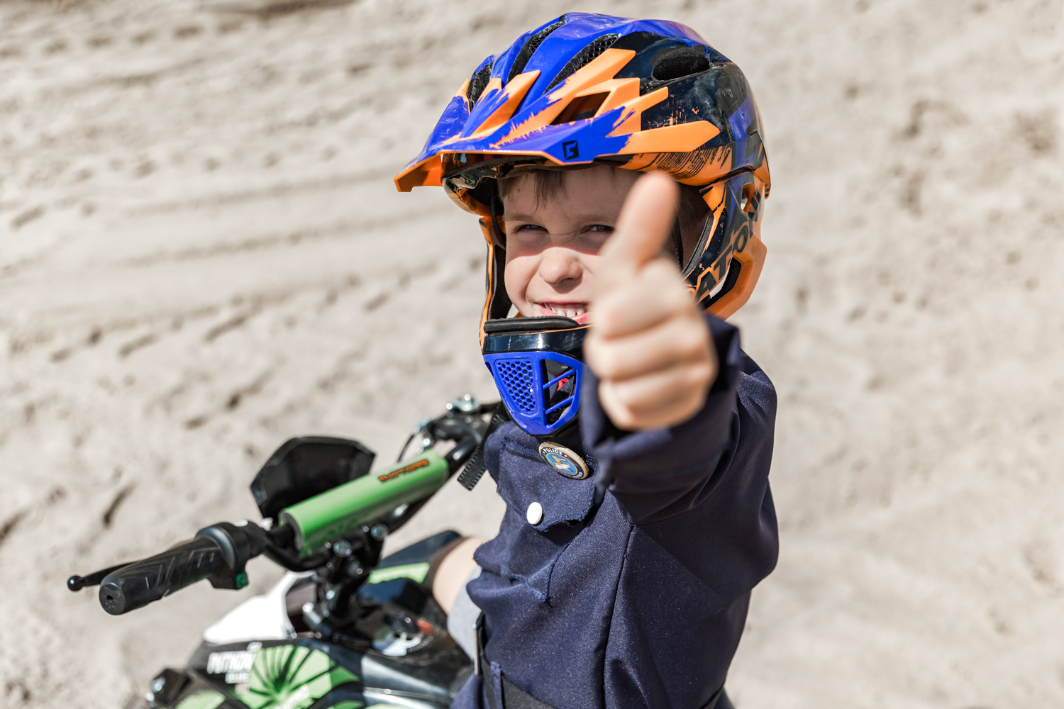 Berniukas su mėlynos ir oranžinės spalvos šalmu iškėlęs nykštį