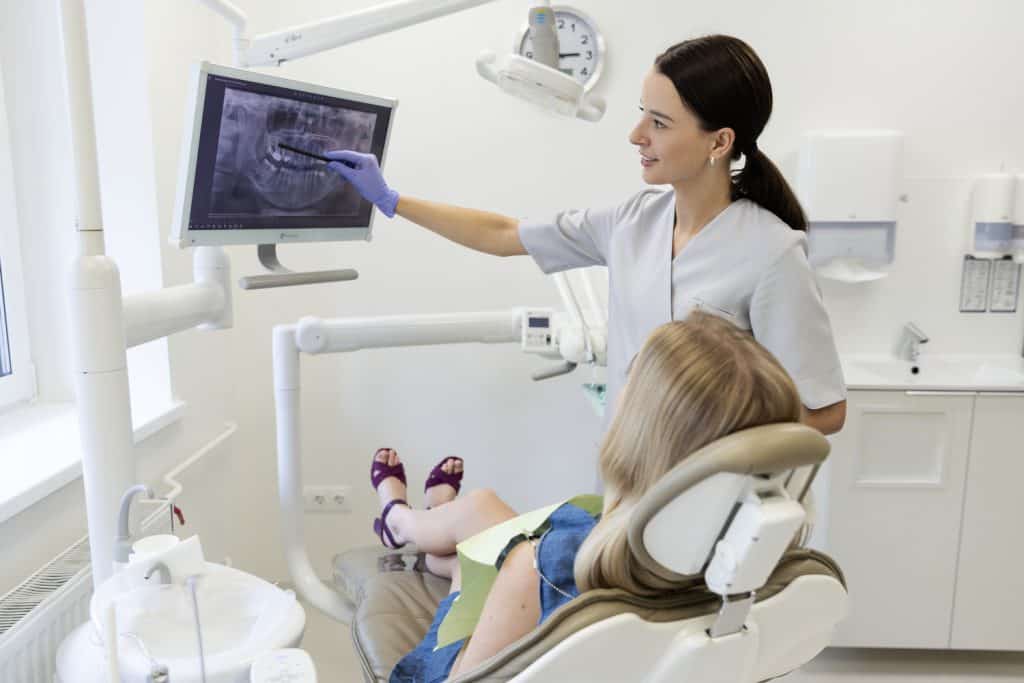 Odontologė rodo rentgeno nuotrauką pacientei klinikos kabinete