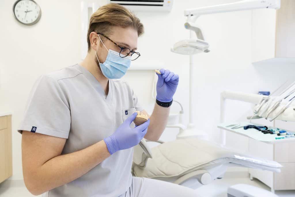 Odontologas su kauke ir pirštinėmis klinikos kabinete
