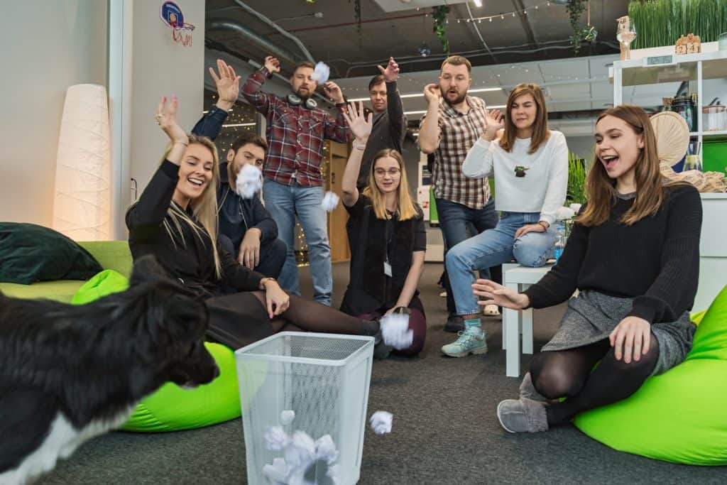Komandos fotosesija biure: kolegos juokiasi ir mėto popieriaus rutuliukus